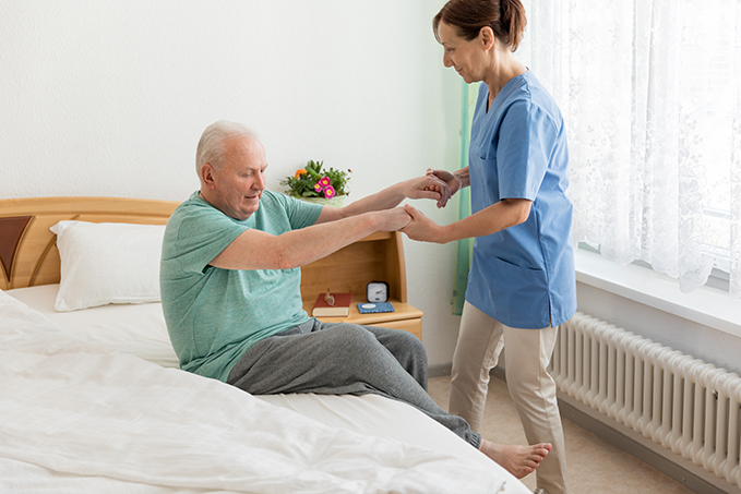 Caregiver assisting senior man getting out of bed